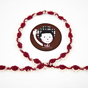 May include: Burgundy and cream colored trim with a knotted design. The trim is made of fabric and is approximately 1/2 inch wide.