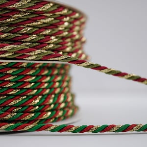 Puede incluir: Carretes de cordón trenzado decorativo en colores navideños. El cordón presenta un diseño en espiral con hilos metálicos rojos, verdes y dorados. Los carretes están bien enrollados, mostrando la textura y las variaciones de color del cordón. Ideal para manualidades y decoraciones festivas.