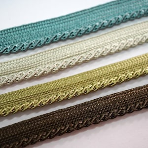 Könnte beinhalten: Nahaufnahme von vier dekorativen Zierbändern in Türkis, Creme, Gold und Braun. Jedes Band hat eine gewebte Textur mit einem gewellten Rand. Ideal zum Basteln und Hinzufügen von Details zu Stoffprojekten.