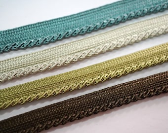 Könnte beinhalten: Nahaufnahme von vier dekorativen Zierbändern in Türkis, Creme, Gold und Braun. Jedes Band hat eine gewebte Textur mit einem gewellten Rand. Ideal zum Basteln und Hinzufügen von Details zu Stoffprojekten.