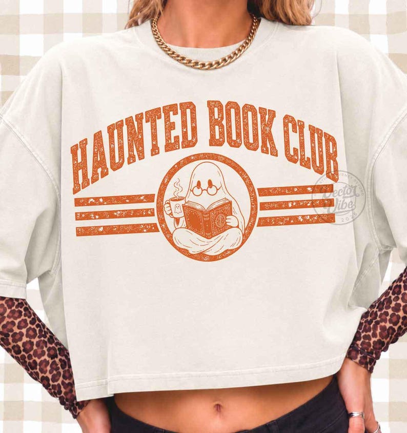 Puede incluir: Una camiseta corta de color blanco roto con un gr&aacute;fico naranja desgastado que dice "HAUNTED BOOK CLUB" en fuente arqueada. El dise&ntilde;o incluye un fantasma con gafas, leyendo un libro y sosteniendo una taza, flanqueado por rayas horizontales.