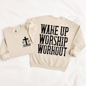 Puede incluir: Dos sudaderas beige. Una tiene un gr&aacute;fico de cruz y barra con la palabra "EVERYDAY". La otra tiene las palabras "WAKE UP WORSHIP WORKOUT" en letras negras grandes. Las sudaderas est&aacute;n sobre un fondo blanco.