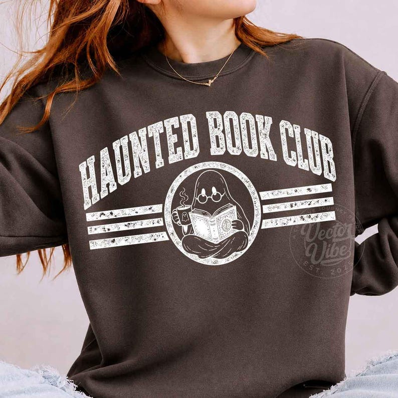 Puede incluir: Una sudadera de cuello redondo gris oscuro con un gr&aacute;fico blanco desgastado que dice HAUNTED BOOK CLUB en fuente arqueada. El dise&ntilde;o incluye un emblema circular central de un fantasma con gafas, sosteniendo una taza humeante y un libro abierto.