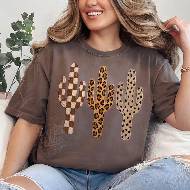 May include: A brown t-shirt with three cactus designs. The cacti feature a checkered pattern, a leopard print, and a dotted design. The shirt has the text "Vector Vibe Est 2025" at the bottom.