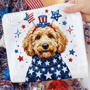 Pode incluir: Uma almofada quadrada branca com uma ilustração de um cão com um chapéu e um suéter patrióticos. O cão tem pelo castanho e é rodeado por estrelas vermelhas, brancas e azuis. A almofada tem o texto "Dee Vibe Est. 2015".