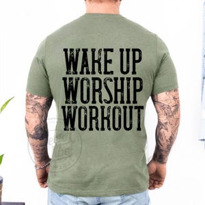 Puede incluir: Camiseta verde oliva con el texto "WAKE UP WORSHIP WORKOUT" en una fuente negra desgastada. La camiseta es de cuello redondo y parece estar hecha de un material suave. La parte trasera de la camiseta es visible.