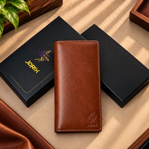 May include: A rectangular brown leather wallet with a smooth finish and a small embossed logo at the bottom right corner. The wallet is positioned vertically between two black rectangular boxes, one of which features the yellow text JORIX.