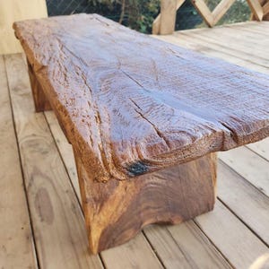 May include: A brown, wooden bench with a natural, live edge. The bench is made from a single piece of wood, displaying the grain and texture. The bench has a smooth, polished surface.