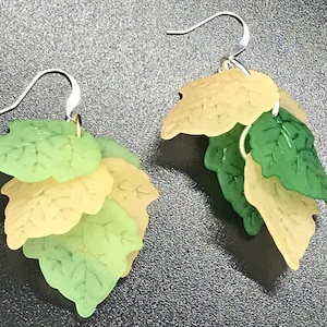 Puede incluir: Un par de pendientes colgantes con múltiples capas de hojas verdes y beige. Las hojas están hechas de un material translúcido y tienen un diseño delicado y en capas.