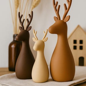 Puede incluir: Tres figuras de ciervo con acabado mate y liso en tonos marr&oacute;n, beige y crema. Cada ciervo presenta un cuerpo redondeado en forma de gota, orejas puntiagudas y astas ramificadas. Las figuras est&aacute;n dispuestas en fila mostrando tonos tierra.