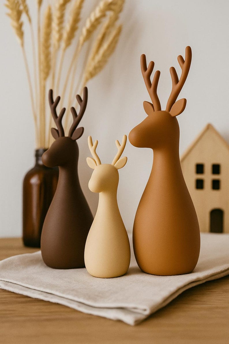 Puede incluir: Tres figuras de ciervo con acabado mate y liso en tonos marr&oacute;n, beige y crema. Cada ciervo presenta un cuerpo redondeado en forma de gota, orejas puntiagudas y astas ramificadas. Las figuras est&aacute;n dispuestas en fila mostrando tonos tierra.
