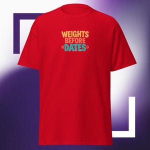 May include: A red t-shirt with the text "WEIGHTS BEFORE DATES" in a colorful, retro font. The shirt is a solid red color and has a crew neck. The text is in orange, yellow, teal, and white.