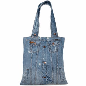 Puede incluir: Un bolso tote de mezclilla azul con dos asas. La bolsa está hecha de una chaqueta de mezclilla reutilizada, con bolsillos, botones y detalles desgastados. La bolsa rectangular está diseñada para transportar objetos.