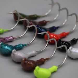 May include: An assortment of colorful fishing jig heads with silver hooks. The jig heads are painted in various colors, including green, purple, teal, white, brown, black, red, and blue. The hooks are made of silver-colored metal.