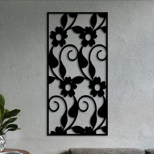 May include: A rectangular black wall panel featuring a laser-cut design of repeating floral motifs, swirling vines, and pointed leaves. The flat, solid black silhouette is framed by a thin border, creating a continuous pattern of organic shapes.