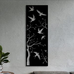 Op de afbeelding: Een hoog, rechthoekig zwart wandpaneel met een zilverkleurig uitgesneden ontwerp van een boom met uitgestrekte takken en verschillende vogels in de vlucht. De metallic zilveren silhouetten van de vogels en de boom contrasteren met de zwarte achtergrond.