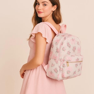 Puede incluir: Una mochila rosa claro con un estampado floral y de lazos. La mochila tiene un bolsillo frontal con cremallera dorada y correas ajustables. Fabricada con un material suave y duradero.