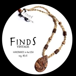 May include: Handmade necklace with a teardrop-shaped pendant and wooden beads. The necklace is made of a woven, tan-colored cord. The tag reads "FINDS VINTAGE" and "HANDMADE in the USA".