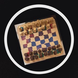May include: A handmade wooden chess set with a painted checkered board in shades of blue, red, and purple. The chess pieces are light brown and dark brown. The set is displayed on a black background.