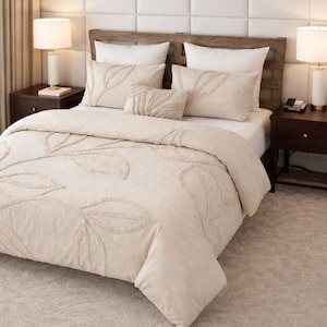 May include: Beige bedding set with leaf pattern embroidery. The set includes a comforter, pillows, and a decorative lumbar pillow. The bed is set against a neutral-toned wall and a matching rug.