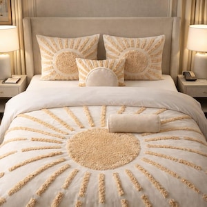 May include: Cream-colored bedding set featuring a sunburst design. The set includes a comforter, pillows, and a bolster pillow. The sunburst design is created with textured, raised elements in a light tan color. The bed is set against a neutral-toned wall.