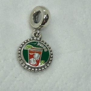 May include: Silver charm with a round pendant featuring a cocktail design. The pendant has a green border with the word "PISCO" and a red cocktail with ice cubes and a lime wedge. A perfect accessory for a charm bracelet.