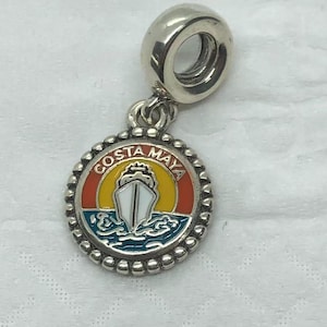 May include: Silver-toned charm with a round pendant featuring the words "COSTA MAYA" and a ship design. The pendant has a colorful background with orange, yellow, and blue hues, and a beaded border.