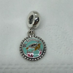 May include: A silver charm with a round pendant featuring a sea turtle design. The pendant has a turquoise background with the words "St. Thomas" around the edge. The turtle is brown and yellow, with red and pink coral accents.