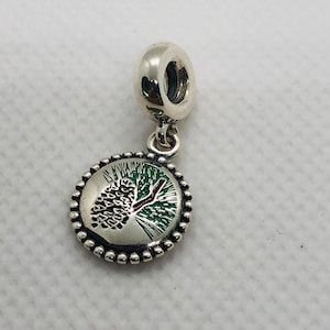 May include: A silver charm featuring a circular pendant with a beaded edge. The center displays an enameled design of a pinecone on a branch with green needles and a brown stem against a silver background. The charm has a round bail for attachment.