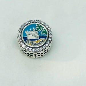 Puede incluir: Un charm redondo de plata con un diseño de crucero. El charm presenta una escena de esmalte azul y verde con un crucero blanco y las palabras "St. Maarten". El charm está rodeado de cristales transparentes.