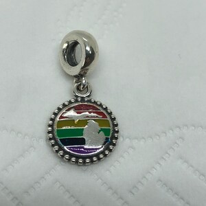 Puede incluir: Un charm de plata con un colgante circular de borde perlado. El centro muestra un fondo de esmalte con rayas de arcoíris y una silueta plateada del estado de Michigan y su península superior superpuesta sobre las franjas de colores.