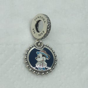 Op de afbeelding: Een zilveren Pandora-bedel met een Mickey Mouse-ontwerp. De bedel heeft een ronde, marineblauwe emaille hanger met een cartoon Mickey Mouse met een hoed en gestreepte outfit. De bedel heeft een kralenrand en een zilveren lus met het Pandora-logo en sprankelende accenten.