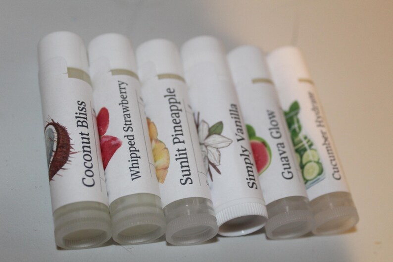 May include: Six white lip balm tubes with labels displaying illustrations of coconut, strawberry, pineapple, vanilla, guava, and cucumber. The lip balms are angled, highlighting the different flavours.