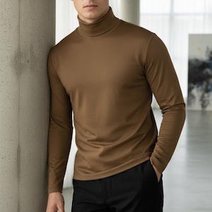 May include: A long-sleeved, brown turtleneck shirt. The shirt is made of a smooth, solid-colored fabric. The model is wearing black pants. The shirt has a high, close-fitting neckline and long sleeves.
