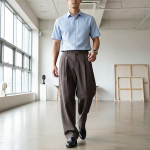 May include: A light blue short-sleeved button-down shirt paired with brown pleated trousers. The outfit is completed with black leather loafers. The person is walking in a bright, open space with large windows.