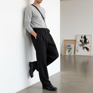 Peut inclure: Une personne porte un haut gris &agrave; manches longues et un pantalon noir. Le pantalon a un devant pliss&eacute; et est associ&eacute; &agrave; des chaussures en cuir noir. Un sac &agrave; bandouli&egrave;re noir est port&eacute; en travers de l'&eacute;paule.