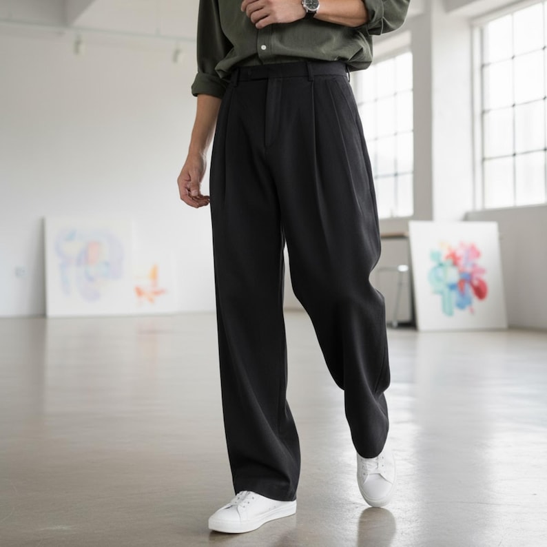 Peut inclure: Pantalon noir &agrave; jambes larges avec des plis. Le pantalon est associ&eacute; &agrave; des baskets blanches et &agrave; une chemise verte boutonn&eacute;e. Le mod&egrave;le se tient dans un espace lumineux et ouvert avec des &oelig;uvres d'art.
