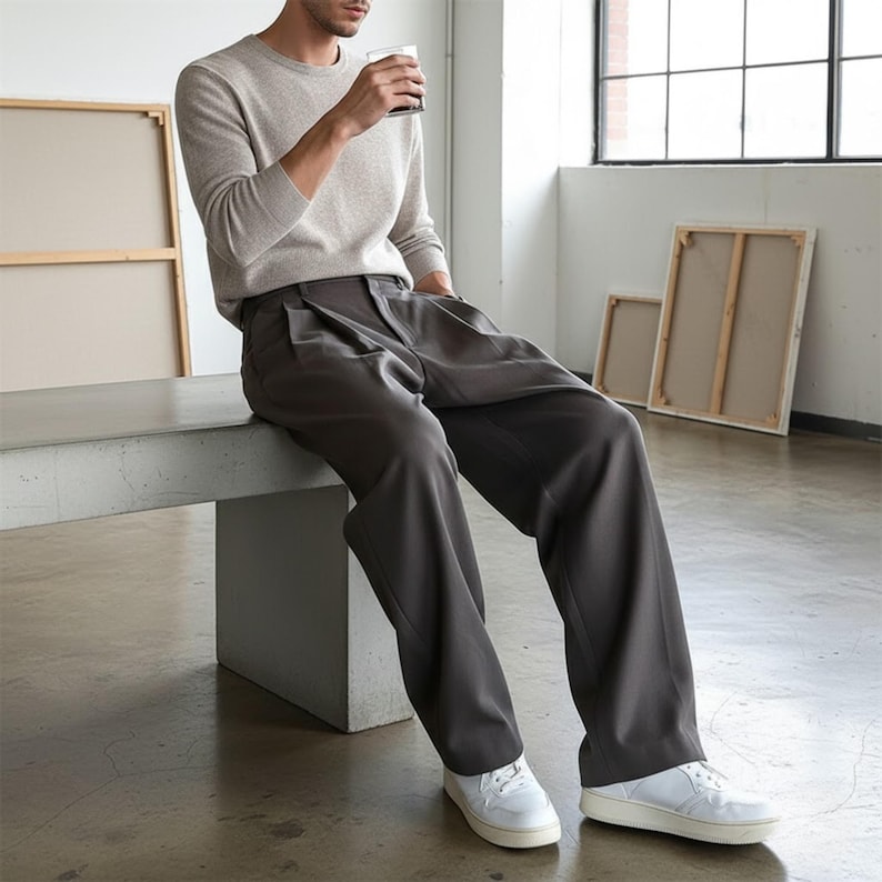 Peut inclure: Une personne portant un pull ras du cou beige clair et un pantalon pliss&eacute; gris fonc&eacute;. La personne porte des baskets blanches. Le cadre est une pi&egrave;ce avec de grandes fen&ecirc;tres et des &oelig;uvres d'art.