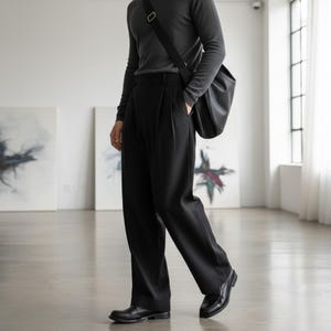 Peut inclure: Une personne porte une chemise grise &agrave; manches longues et un pantalon noir pliss&eacute;. Il porte un sac en bandouli&egrave;re noir et des mocassins en cuir noirs. La tenue est simple et &eacute;l&eacute;gante, adapt&eacute;e au quotidien.