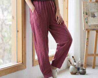 May include: Burgundy-colored linen pants with an elastic waistband and pockets. The pants are paired with a gray top and white sneakers. The casual outfit is suitable for everyday wear.