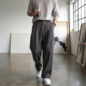 Peut inclure: Une personne portant un pull gris clair et un pantalon pliss&eacute; gris fonc&eacute;. La personne porte des baskets blanches et tient un verre d'une boisson fonc&eacute;e. Le pantalon a une coupe large.