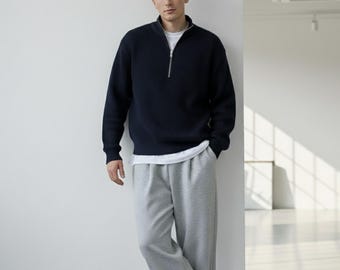 Könnte beinhalten: Ein marineblauer Rippstrickpullover mit silbernem Reißverschluss, getragen über einem weißen T-Shirt, kombiniert mit grauer Jogginghose. Das Outfit ist lässig. Das Model steht vor einer weißen Wand. Der Pullover ist ca. 70 cm lang.