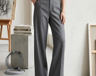 May include: High-waisted grey trousers featuring a wide-leg silhouette, a structured waistband with belt loops, a front zipper fly closure, and a clean, tailored finish. The trousers are crafted from a solid grey fabric with visible vertical seams.