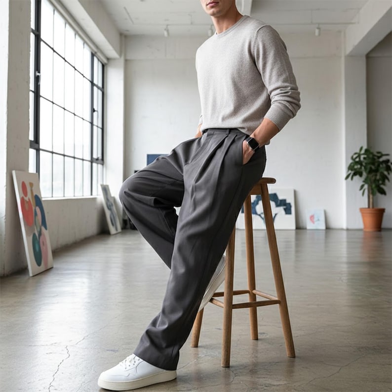 Peut inclure: Un pull ras du cou gris clair et un pantalon pliss&eacute; gris fonc&eacute;. La personne porte une montre noire et des baskets blanches. La personne est assise sur un tabouret en bois dans une pi&egrave;ce lumineuse avec de grandes fen&ecirc;tres.