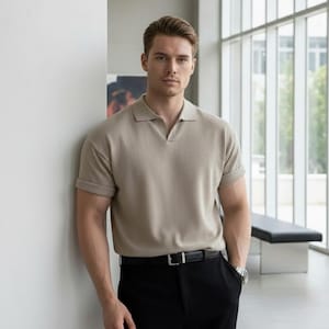 Puede incluir: Polo beige con mangas cortas y cuello en V. La camisa se combina con pantalones negros y un cinturón negro con hebilla plateada. Se ve un reloj plateado en la muñeca.