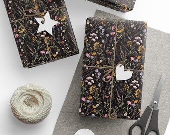 May include: Three wrapped gifts with floral patterned paper, tied with twine and white tags. A ball of twine, scissors, and additional tags are also present, all on a white and gray surface. The gifts are wrapped in black paper with a colorful floral design.