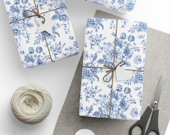 May include: Three wrapped gifts with blue floral patterns on white paper, tied with twine and blank tags. A ball of twine, scissors, and blank tags are also present, suggesting gift wrapping supplies.