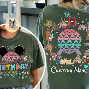 May include: Green t-shirt with a colorful graphic design. The front features a Mickey Mouse head, a geometric shape, and the text "Celebrating My Birthday Around The World." The back has a globe design surrounded by landmarks and characters.
