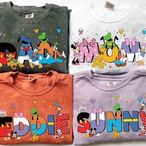 May include: Four crewneck sweatshirts in different colours, each with a Disney character design. The sweatshirts display the words "DAD", "MOM", "EDDIE", and "SUNNY" in colourful, cartoon-style lettering, with Disney characters incorporated.