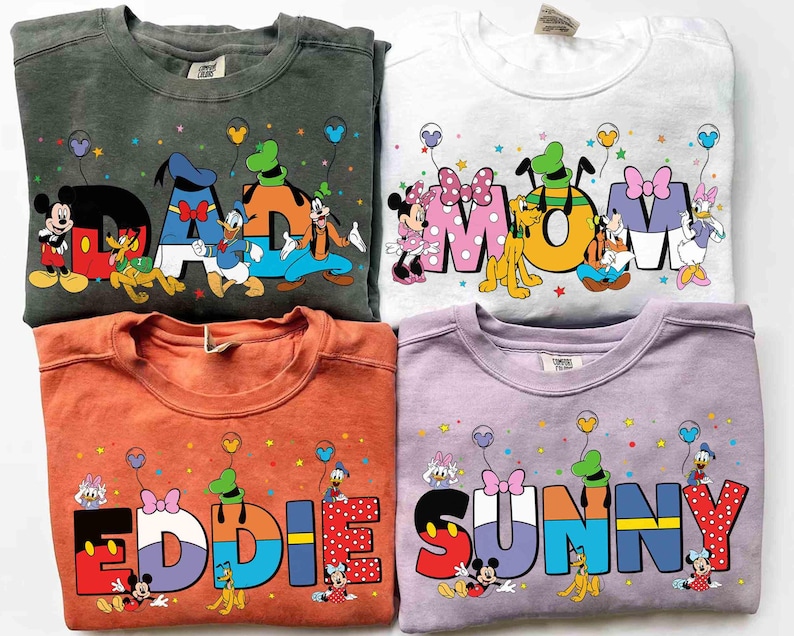 May include: Four crewneck sweatshirts in different colours, each with a Disney character design. The sweatshirts display the words "DAD", "MOM", "EDDIE", and "SUNNY" in colourful, cartoon-style lettering, with Disney characters incorporated.